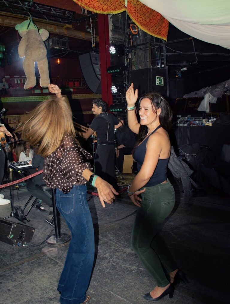 Dos personas bailando ante un pequeño escenario con músicos e iluminación.