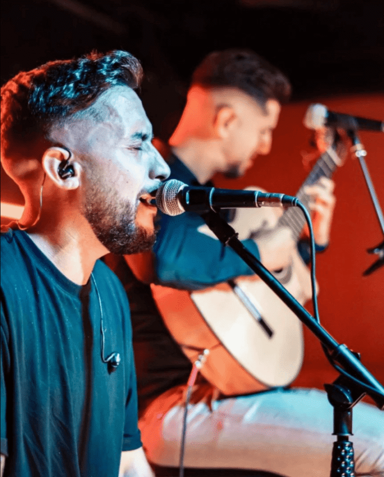 Cantante ante un micrófono con un guitarrista al fondo.