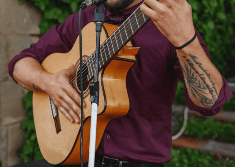 Manos de un músico tocando una guitarra española junto a un micrófono.